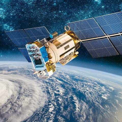 Ein Satellit mit zwei aus Solaranlagen bestehenden Flügeln, kreist um unsere Erde. Die Erde ist als blauer Planet mit einer großen weißen Wolkendecke dargestellt. Der Weltraum im Hintergrund ist dunkelblau und es sind weiß funkelnde Sterne zu sehen. 